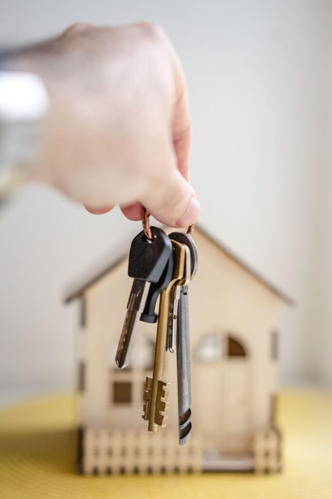 Hand holds out keys with house in the background