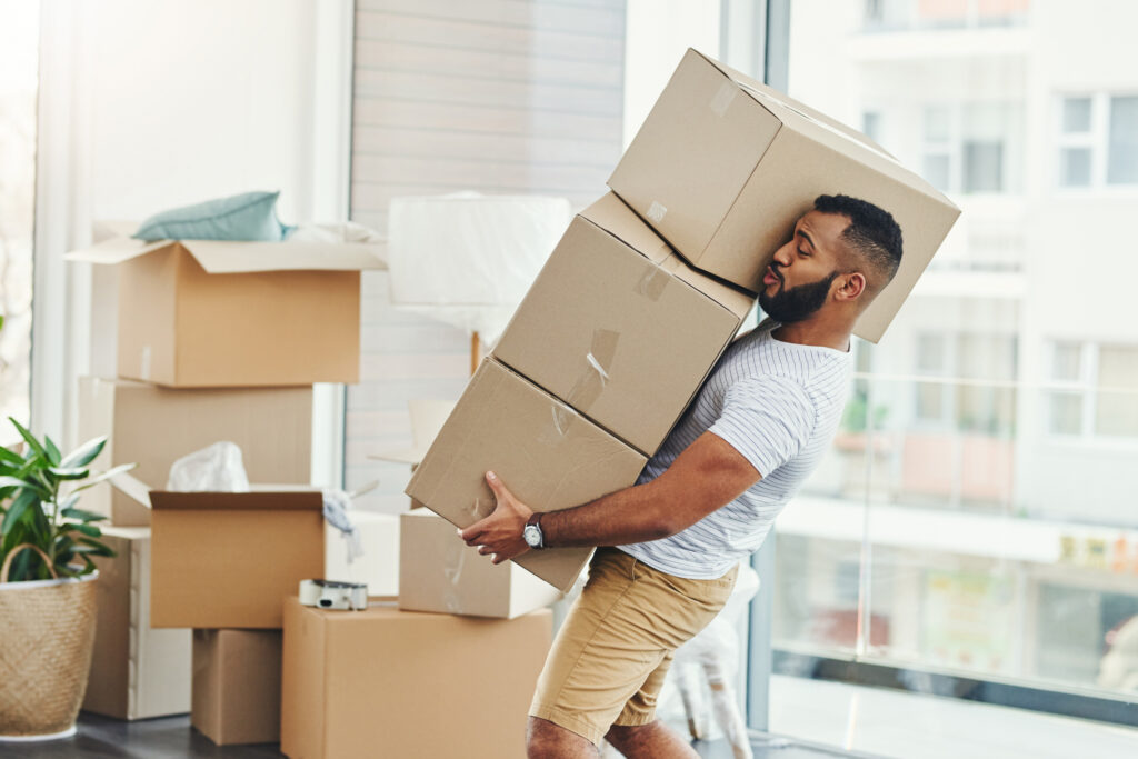 Man carrying a stack of moving boxes in a new apartment, representing a PCS move and military weight allowance limits.
