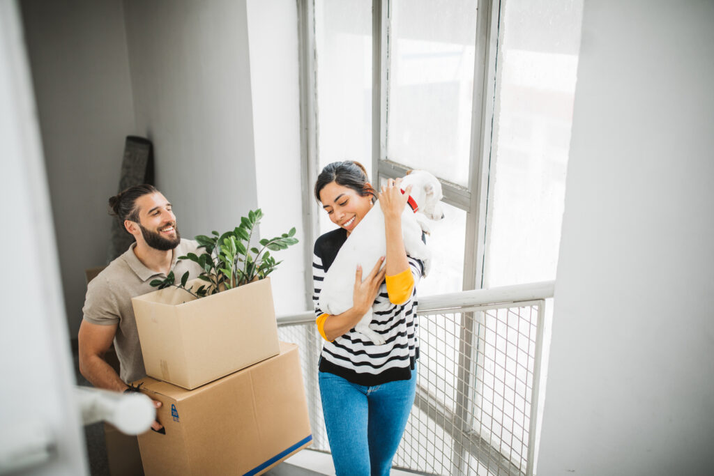 A smiling couple carrying boxes and a dog up a staircase during a DITY move.