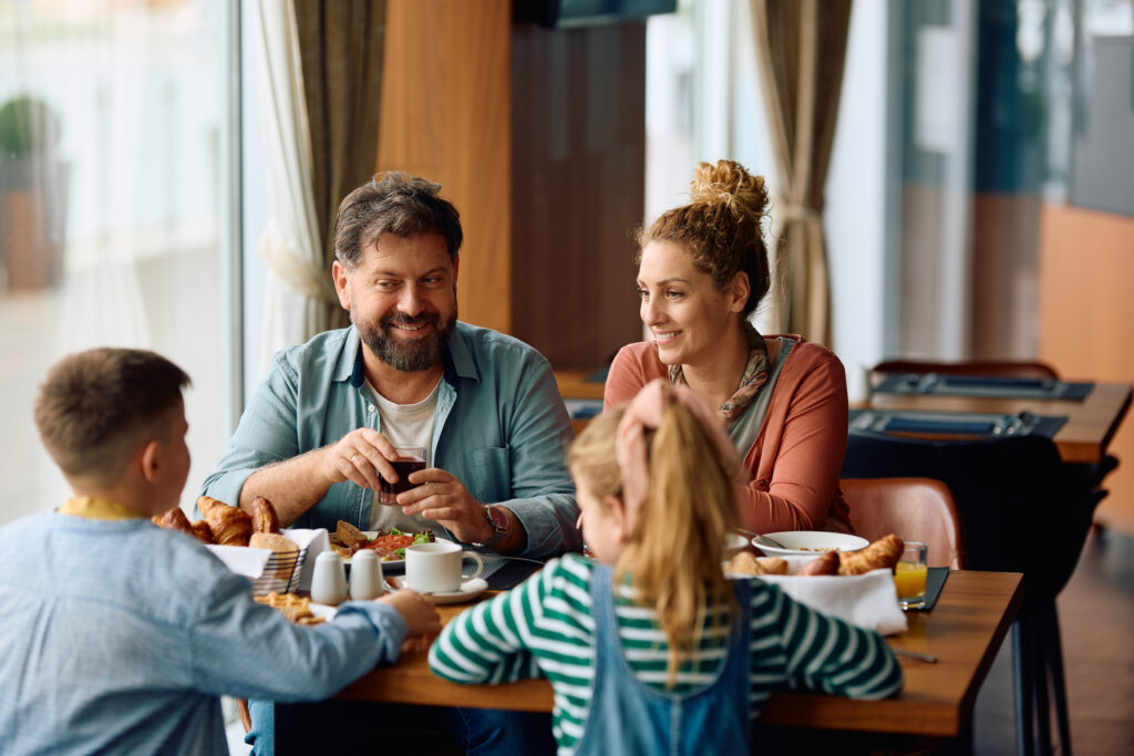 A smiling family enjoys a meal together at a restaurant, representing Veterans and military families dining out with Veterans Day discounts.